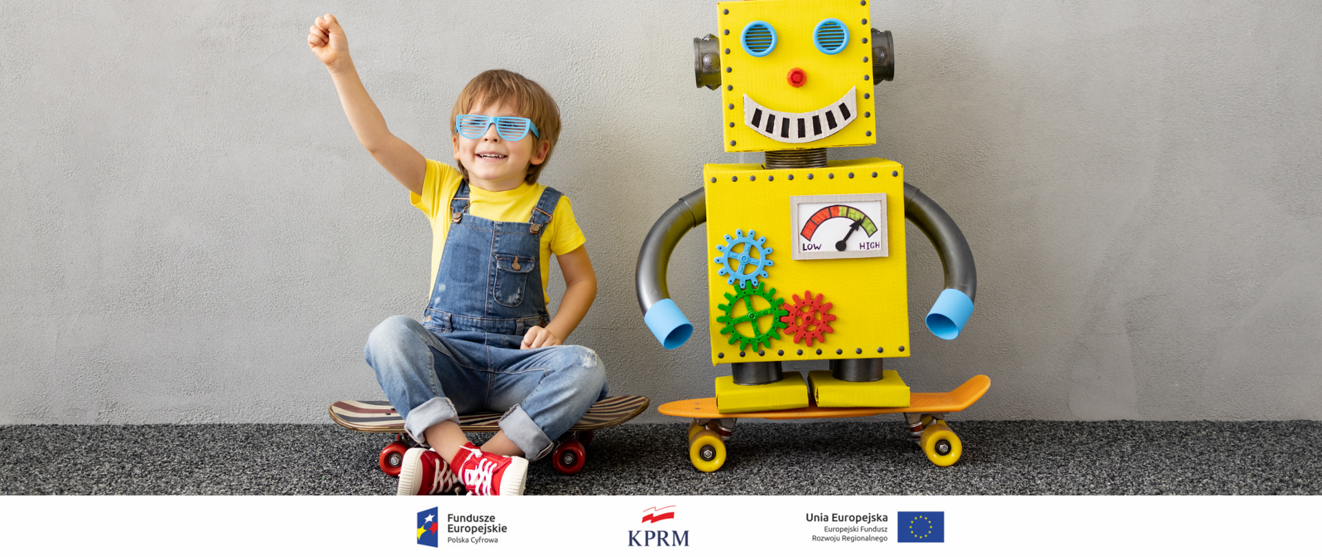 Siedzący na deskorolce chłopiec w żółtej koszulce, jeansowych ogrodniczkach i błękitnych okularach przeciwsłonecznych - uśmiech się szeroko, prawą rękę z radości unosi do góry. Po jego lewej stronie, także na deskorolce, stoi żółty robo wielkości siedzącego chłopca.