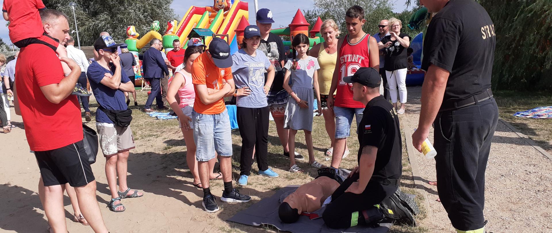 Strażacy PSP pokazują grupie ludzi jak udzielać pierwszej pomocy.