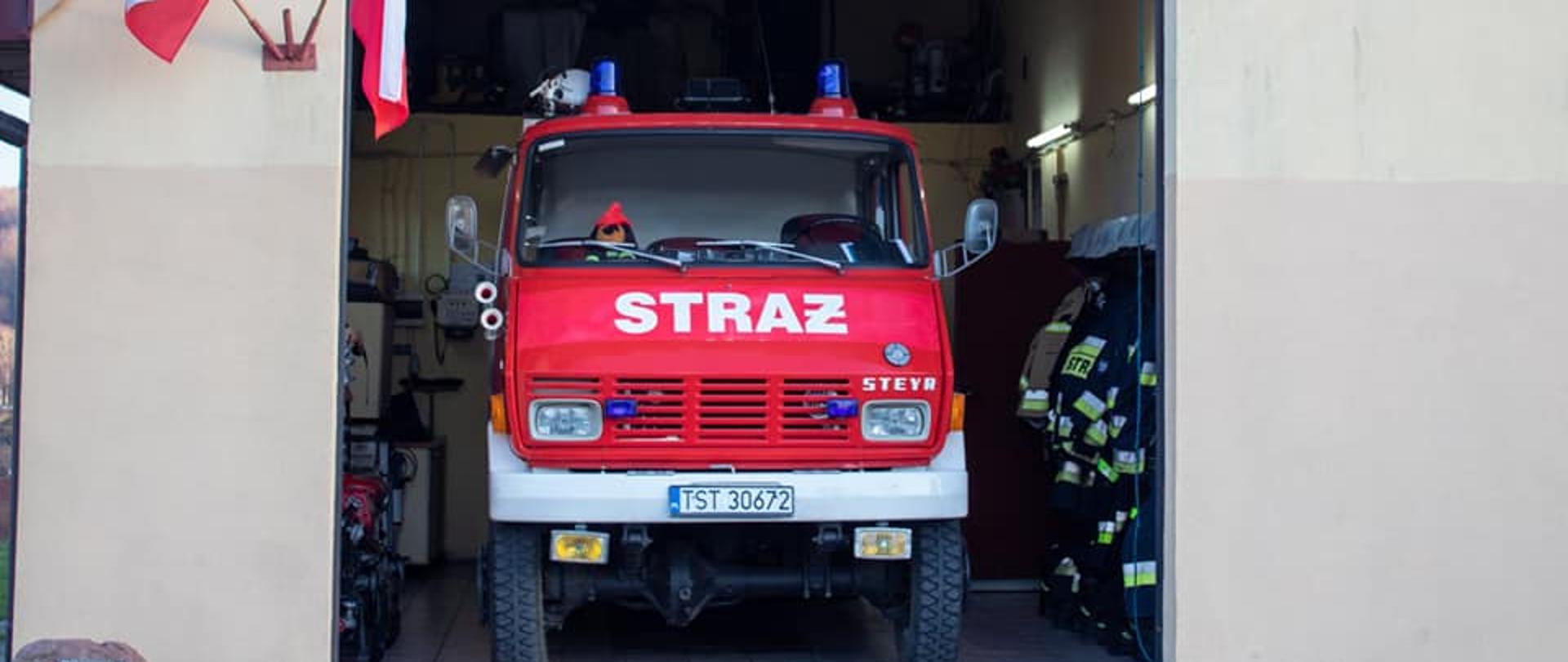 Na pierwszym planie remiza OSP Ruda z otwartym garażem i widocznym czerwonym pojazdem bojowym