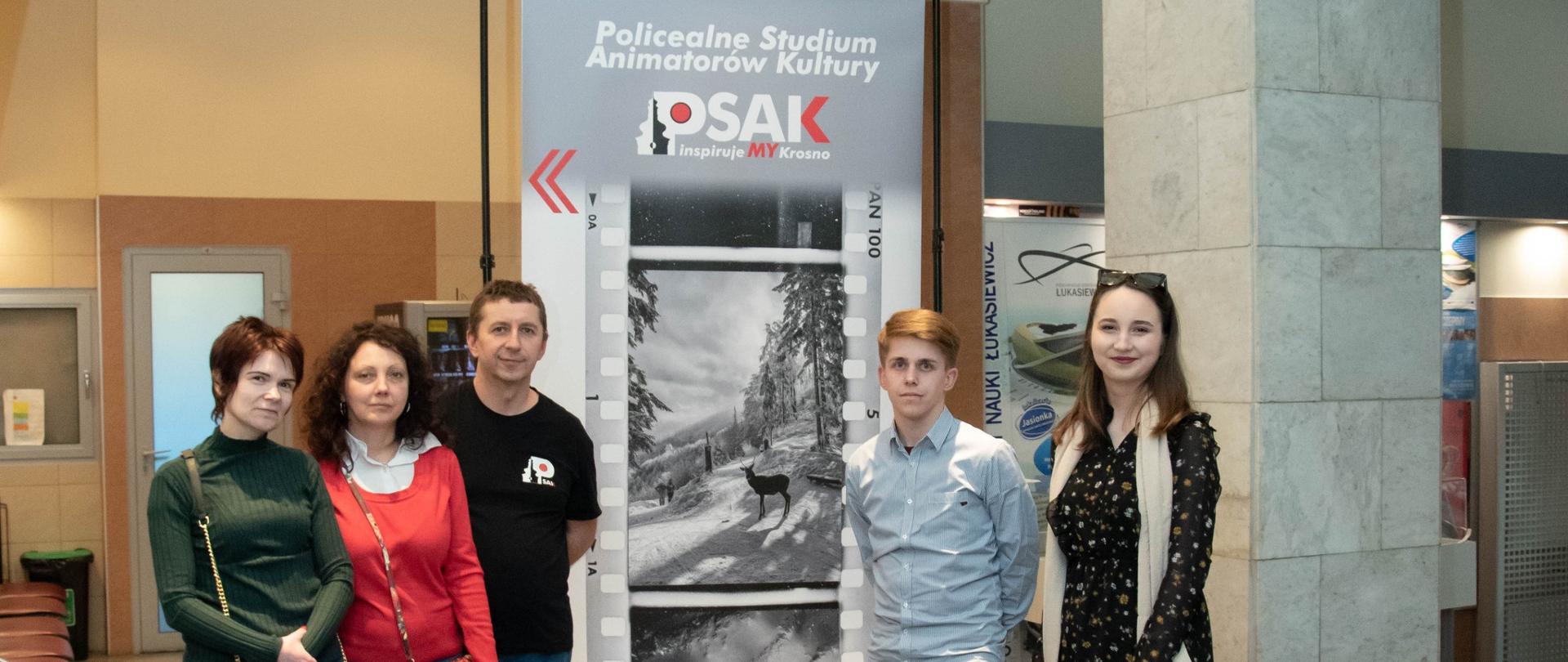 Na zdjęciu słuchacze oraz nauczyciel Studium podczas wernisażu XXI Podkarpackich Konfrontacji Fotograficznych. Pozują na tle banneru reklamowego Studium.