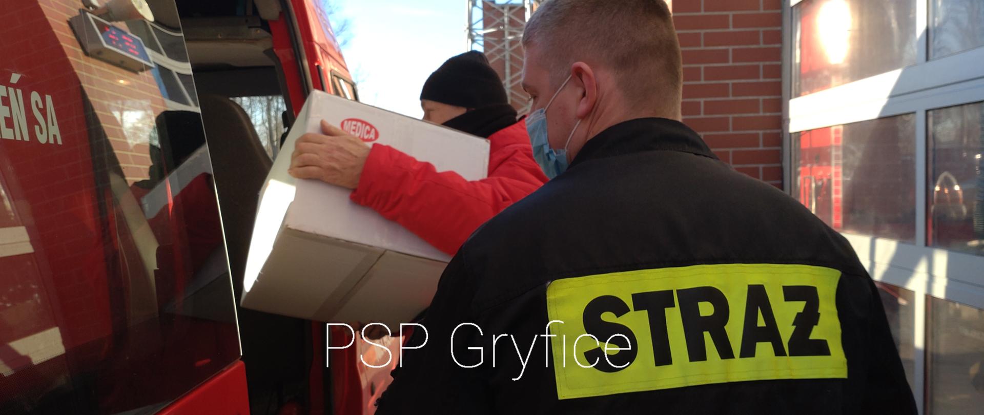 Widoczny na zdjęciu strażak niosący do auta z OSP Niechorze, karton z maseczkami 