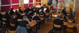 Zawarcie porozumienia. Jedna z klas w Zespole Szkół w Miejskiej Górce. Naprzeciw uczniów siedzących przy stolikach, na tle tablicy i roll-up promocyjnych stoi zastępca komendanta powiatowego PSP, który przekazuje uczniom wiedzę dot. zasad naboru do służby w PSP. Z lewej strony siedzi dyrektor placówki.