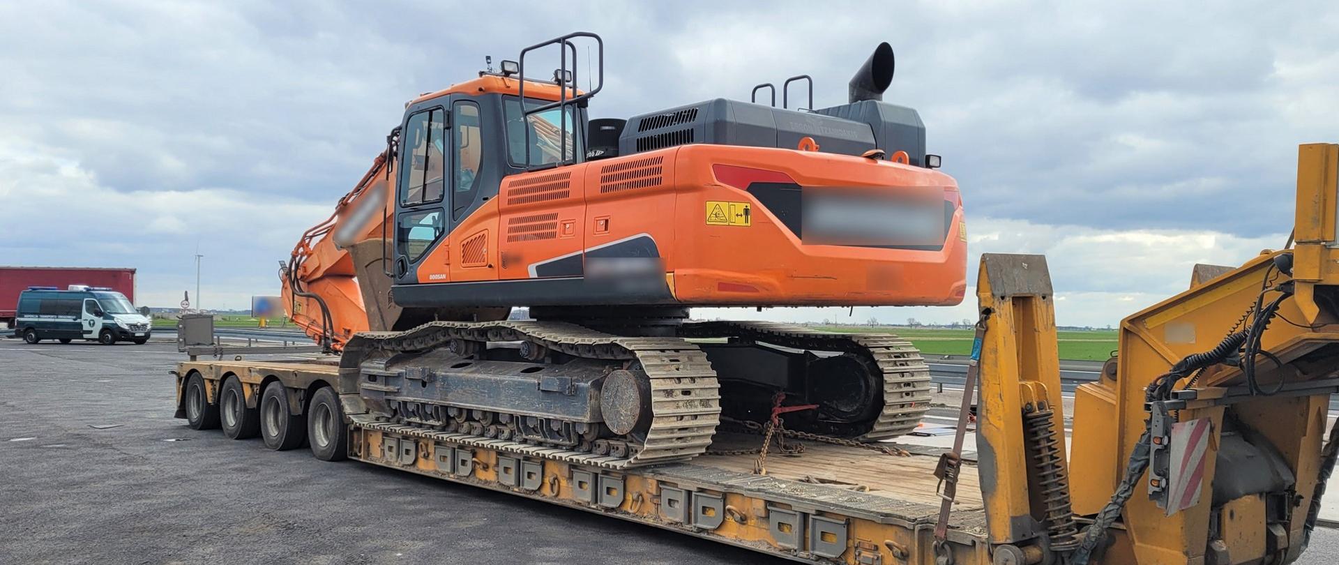 Na pierwszym planie: naczepa niskopodwoziowa z przewożoną dużą koparką gąsienicową. W tle: przód i prawy bok oznakowanego furgonu wielkopolskiej Inspekcji Transportu Drogowego.