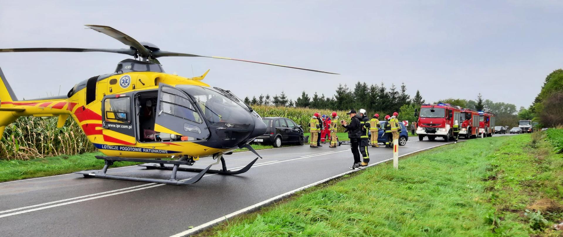 Zdjęcie przedstawia działania podczas wypadku na drodze 106. Na drodze wylądował helikopter LPR oraz stoją wozy straży pożarnej.