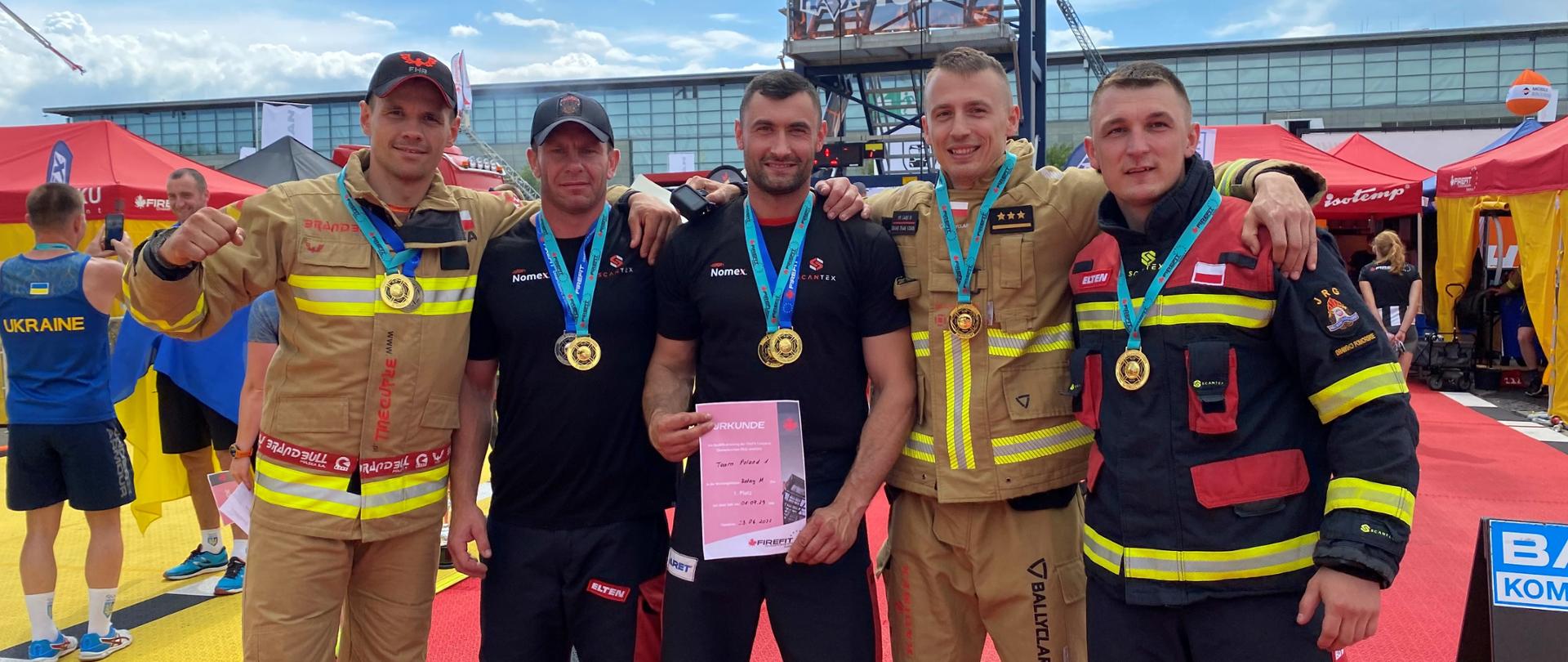 Zdjęcie grupowe pozowane. Polska drużyna składająca się z 5 strażaków, każdy z nich ma zawieszony medal na szyi. Jeden z nich prezentuje dyplom. 
