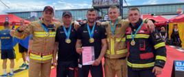 Zdjęcie grupowe pozowane. Polska drużyna składająca się z 5 strażaków, każdy z nich ma zawieszony medal na szyi. Jeden z nich prezentuje dyplom. 