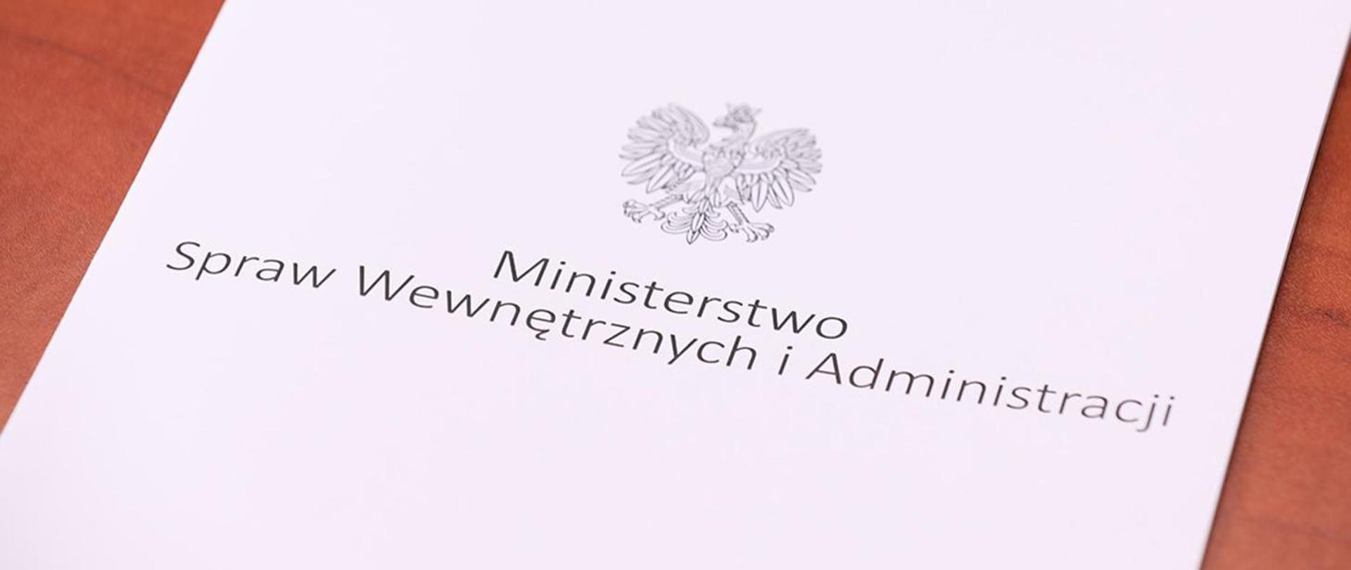 Zdjęcie przedstawia leżącą teczkę z napisem "Ministerstwo Spraw Wewnętrznych i Administracji" i orłem.