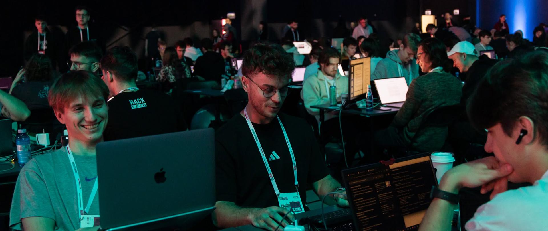 HackNation 2025 - na zdjęciu kilka młodych osób: programiści, specjaliści IT, projektanci, rozwiązujący zadania - wyzwania w ramach wydarzenia 