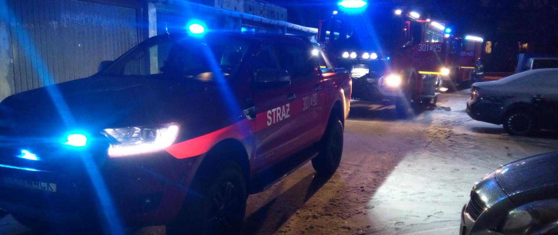 Zdjęcie przedstawia ulicę, przy której zaparkowały trzy samochody pożarnicze biorące udział w likwidacji awarii instalacji ciepłowniczej. Po prawej strony stoją zaparkowane przypadkowe samochody.