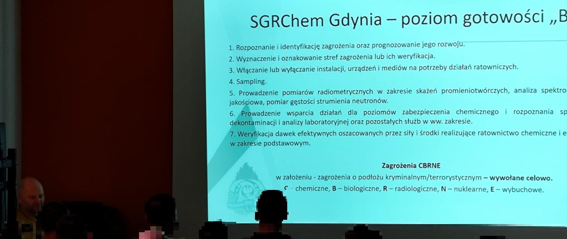 Grupa funkcjonariuszy szkoli się na sali wykładowej. Wyświetlana jest prezentacja na rzutniku.