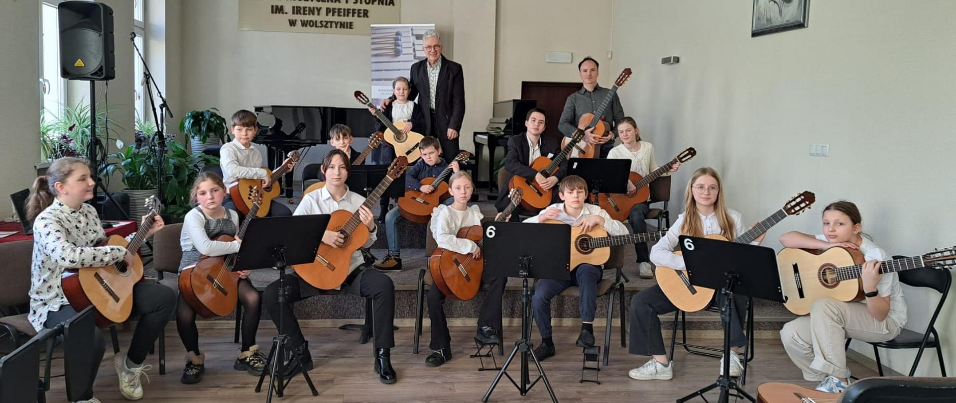 Uczniowie siedzą w półkolu i grają na gitarach.