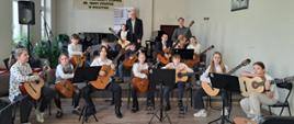 Uczniowie siedzą w półkolu i grają na gitarach