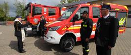 Poświęcenie przez kapelana zachodniopomorskich strażaków, ks. bryg. Ryszarda Szczygła dwóch nowo zakupionych samochodów pożarniczych dla jednostek OSP. W tle widać częściowo zachmurzone niebo.