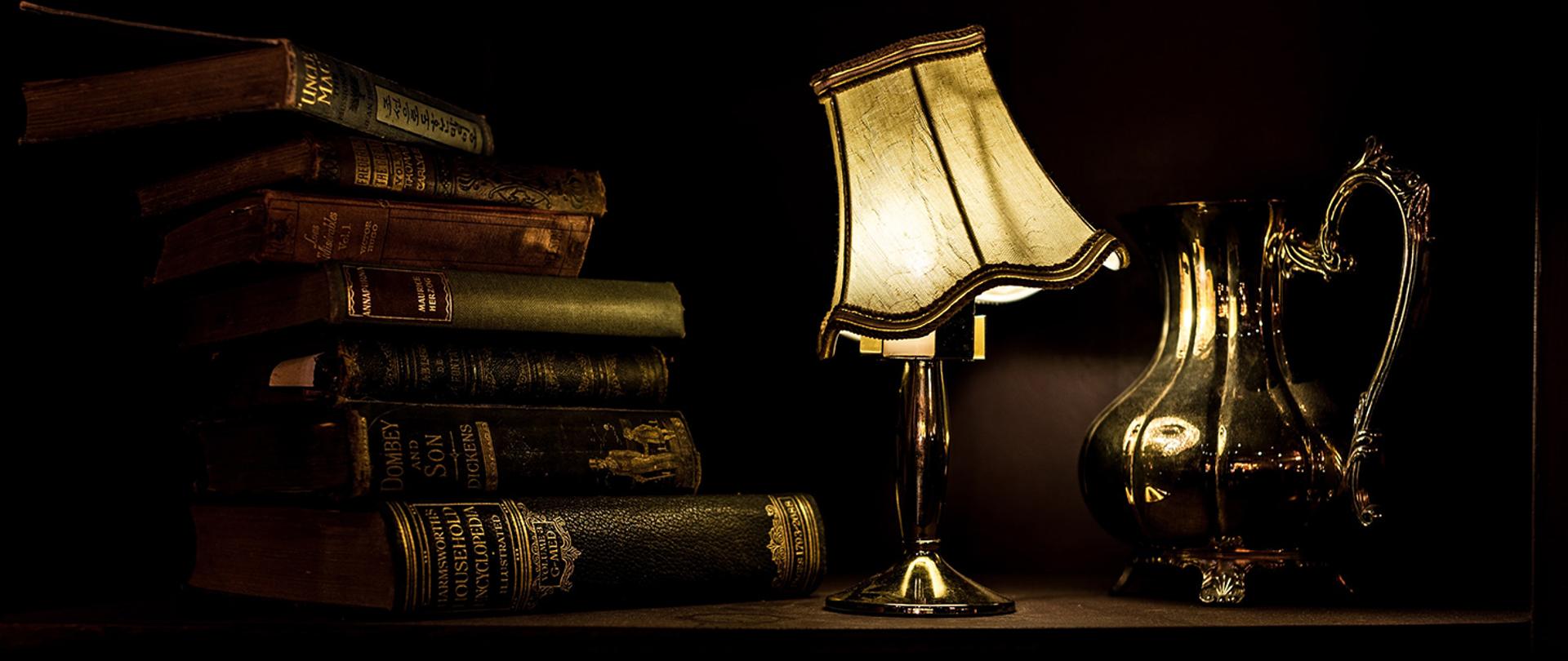 Baner przedstawiający książki, lampę oraz dzban
