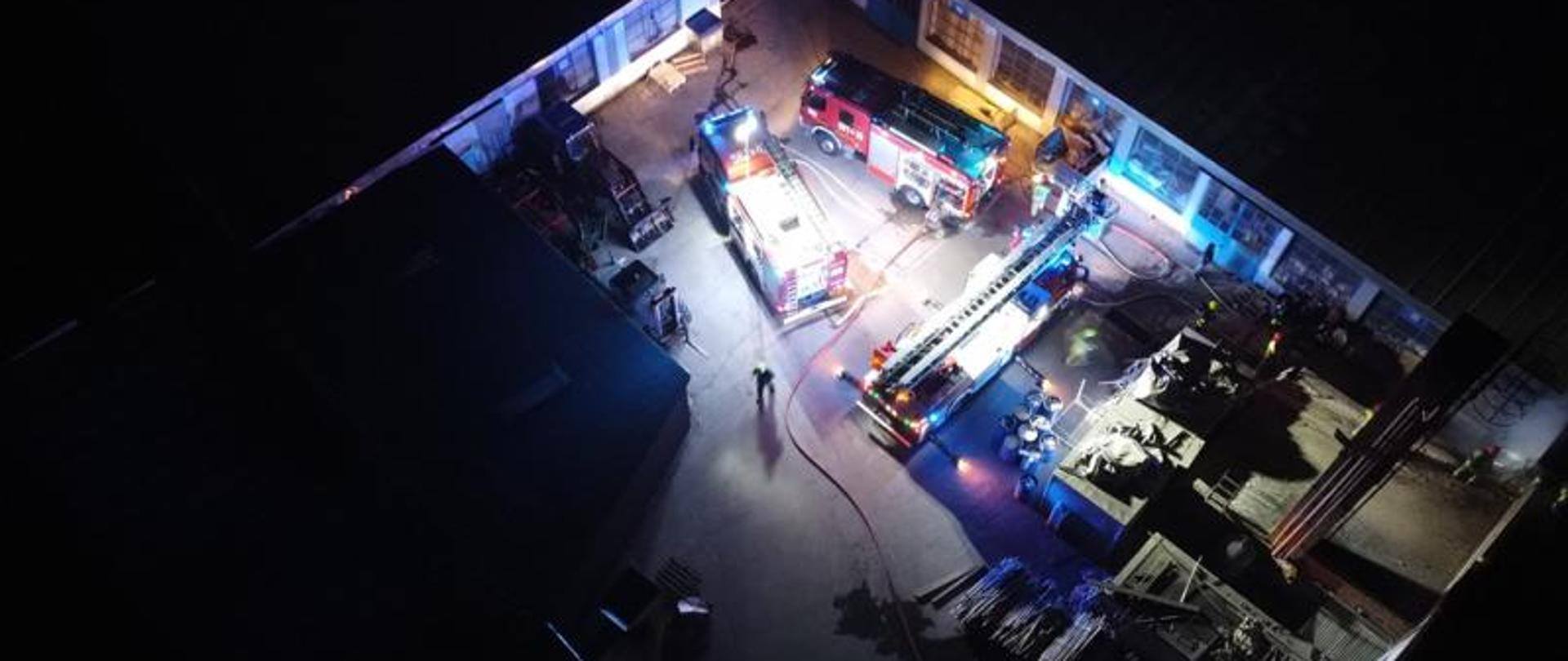 Zdjęcie przedstawia widok z góry na którym widać trzy pojazdy pożarnicze oraz oraz strażaków biorących udział w działaniach gaśniczych.