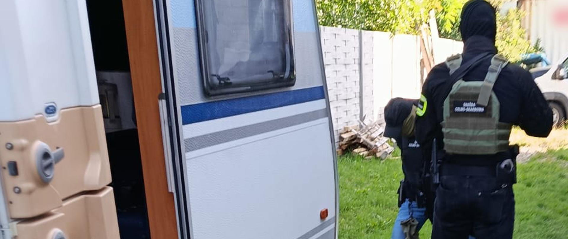Funkcjonariusze Służby Celno-Skarbowej na podwórku, między budynkami obezwładniają podejrzanych mężczyzn.