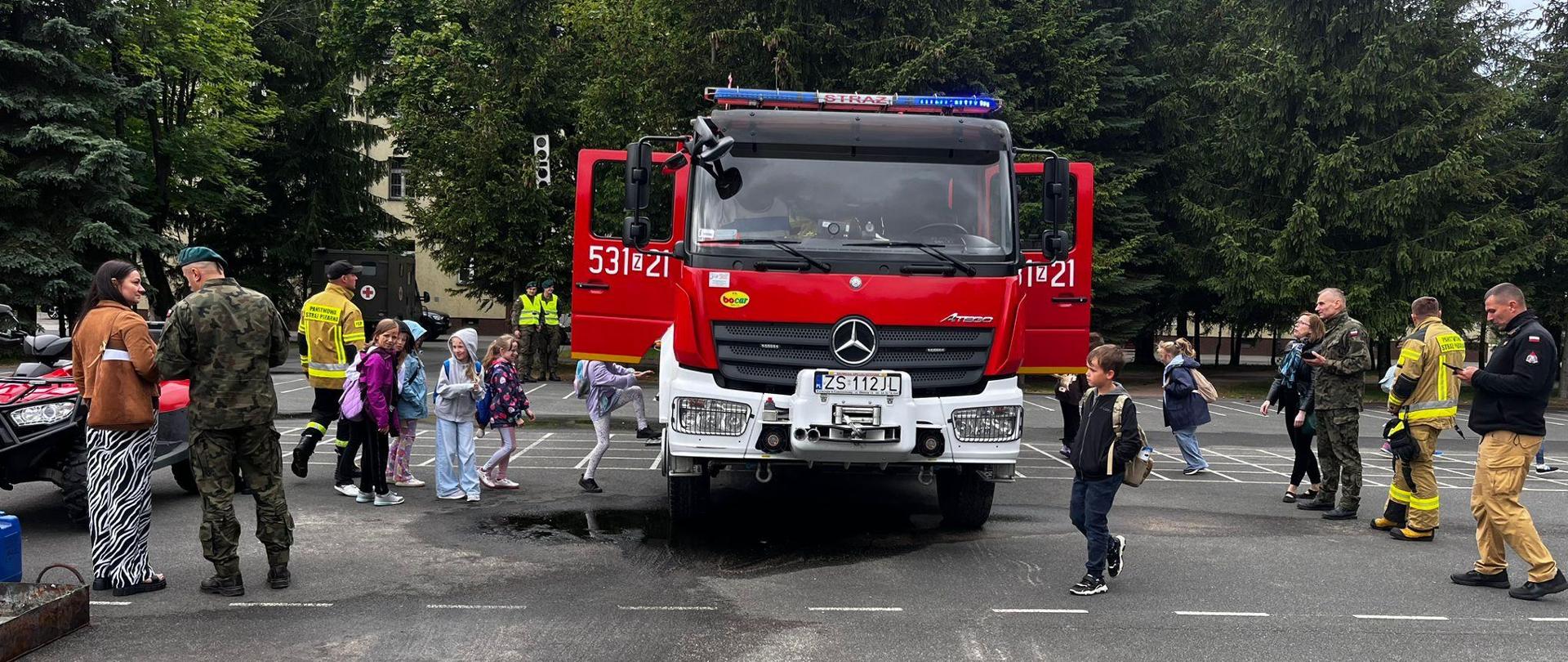 Grupa dzieci wsiada do samochodu strażackiego. wokół widać również strażaków i żołnierzy.