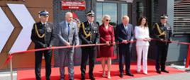Uroczyste przecięcie czerwonej wstęgi przed głównym wejściem do nowego budynku Komendy Powiatowej Państwowej Straży Pożarnej w Garwolinie. W ceremonii biorą udział m.in. Sekretarz Stanu Czesław Mroczek, Starosta Iwona Kurowska oraz wysocy rangą oficerowie PSP w mundurach galowych.