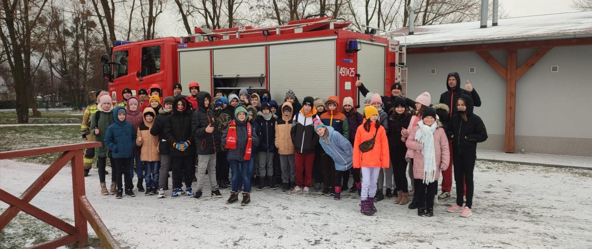 Na zdjęciu znajdują się strażacy oraz uczniowie w tle widać samochód pożarniczy