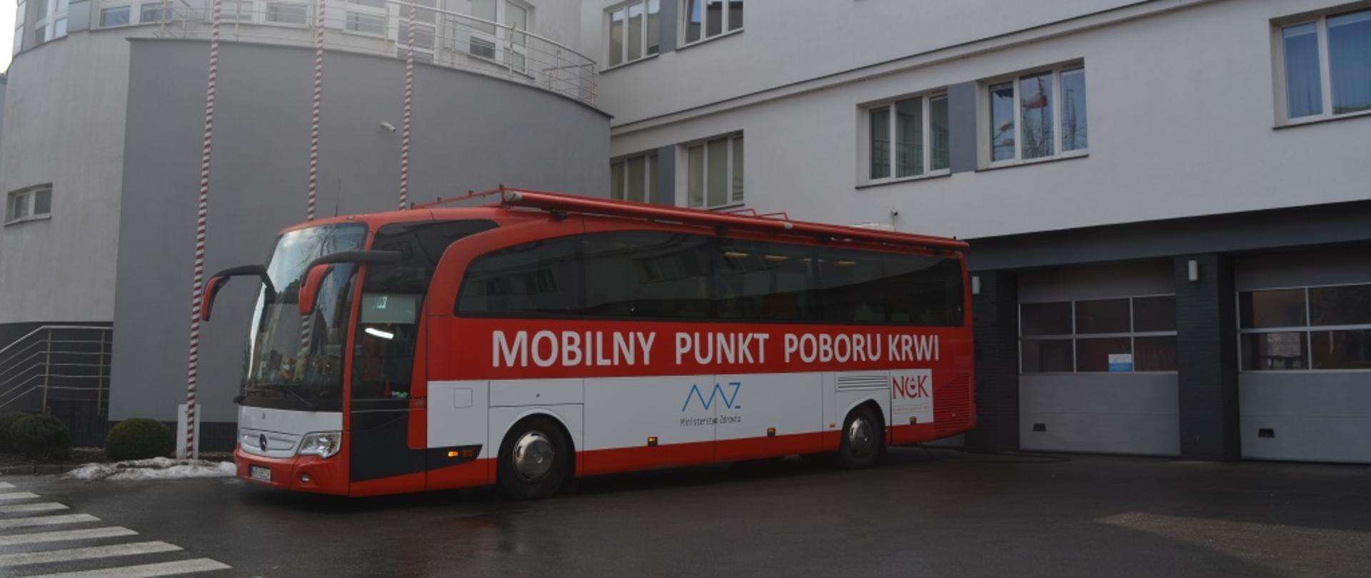 Na zdjęciu widać ustawiony autobus Radomskiego Centrum Krwiodawstwa i Krwiolecznictwa. Autobus w kolorze czerwono - białym. Na boku posiada biały napis mobilny punkt poboru krwi. Zdjęcie wykonane przed bramami garażowymi jednostki ratowniczo - gaśniczej numer 1 w Radomiu. 
