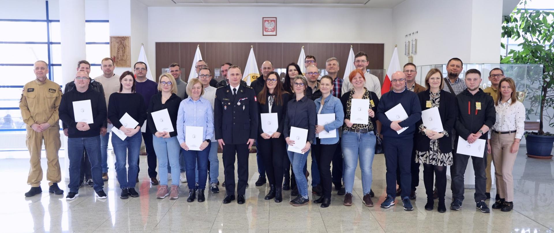 Pamiątkowe zdjęcie grupowe uczestników szkolenia dla inspektorów ochrony przeciwpożarowej (26 osób) w towarzystwie p.o. Komendanta Centralnej Szkoły PSP, kobiety oraz dwóch oficerów CS PSP