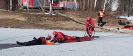 Strażacy za pomocą sań lodowych poruszają się po zamarzniętym akwenie