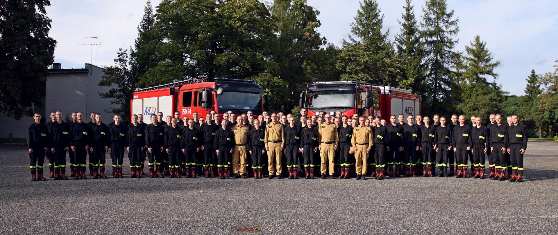 Pamiątkowe zdjęcie kadetów Centralnej Szkoły PSP w towarzystwie Komendanta Głównego PSP Zastępcy Komendanta Głównego PSP oraz Komendanta i Zastępcy Komendanta CS PSP na placu wewnętrznym Szkoły na tle dwóch samochodów bojowych