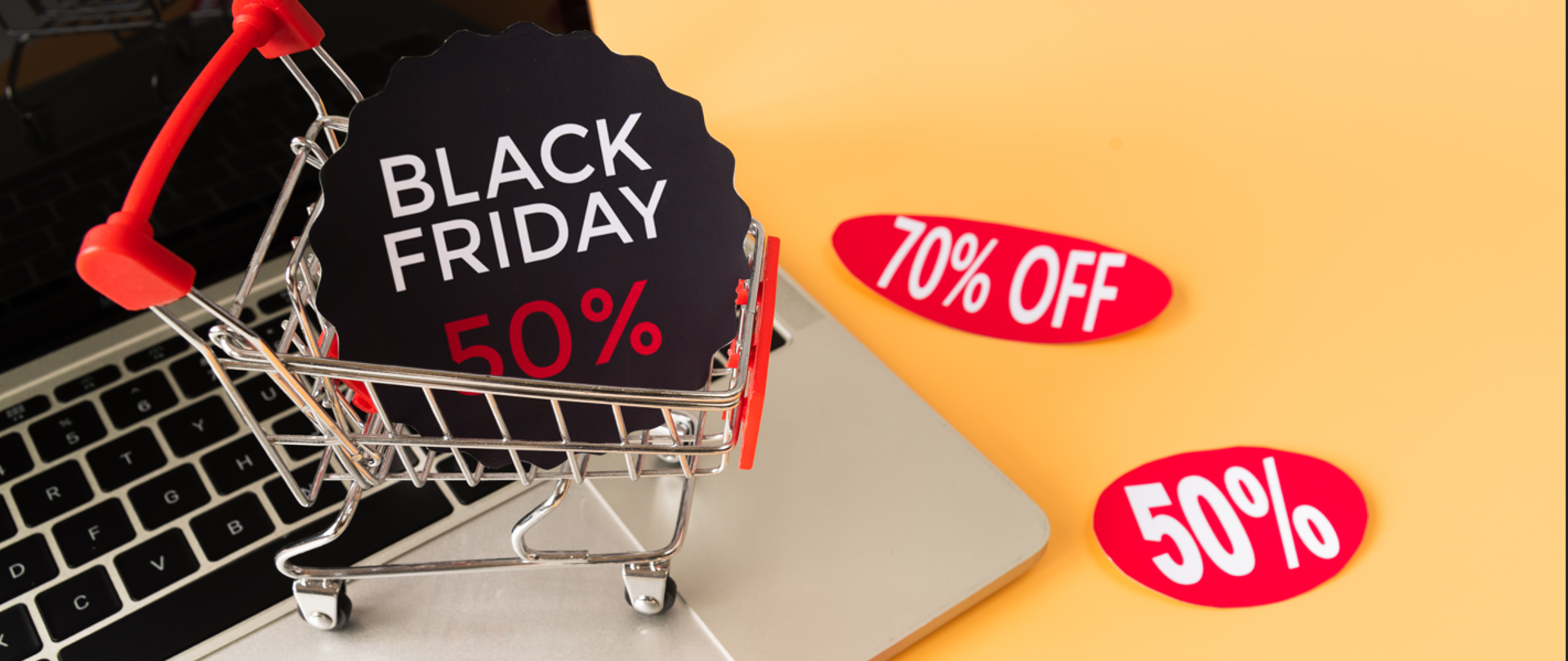 Zdjęcie laptopa na żółtym tle. Na klawiaturze miniatura koszyka zakupowego a w nim napis Black Friday