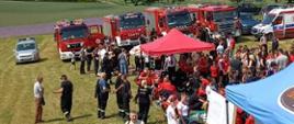 Zdjęcie przedstawia samochody pożarnicze, rozstawione namioty oraz strażaków i zebranych gosci podczas zawodów sportowo - pożarniczych
