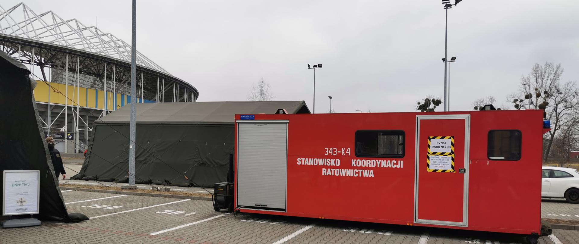 na zdjęciu widać 2 namioty wojskowe, które służą jako punkt poboru wymazu do badania na Covid -19. Obok namiotów stoi kontener dowódczo – sztabowy z Bazy kontenerowej „Kopernik” w Toruniu służący, jako punkt ewidencyjny. Punkt poboru wymazów znajduje się na parkingu przy Motoarenie w Toruniu.