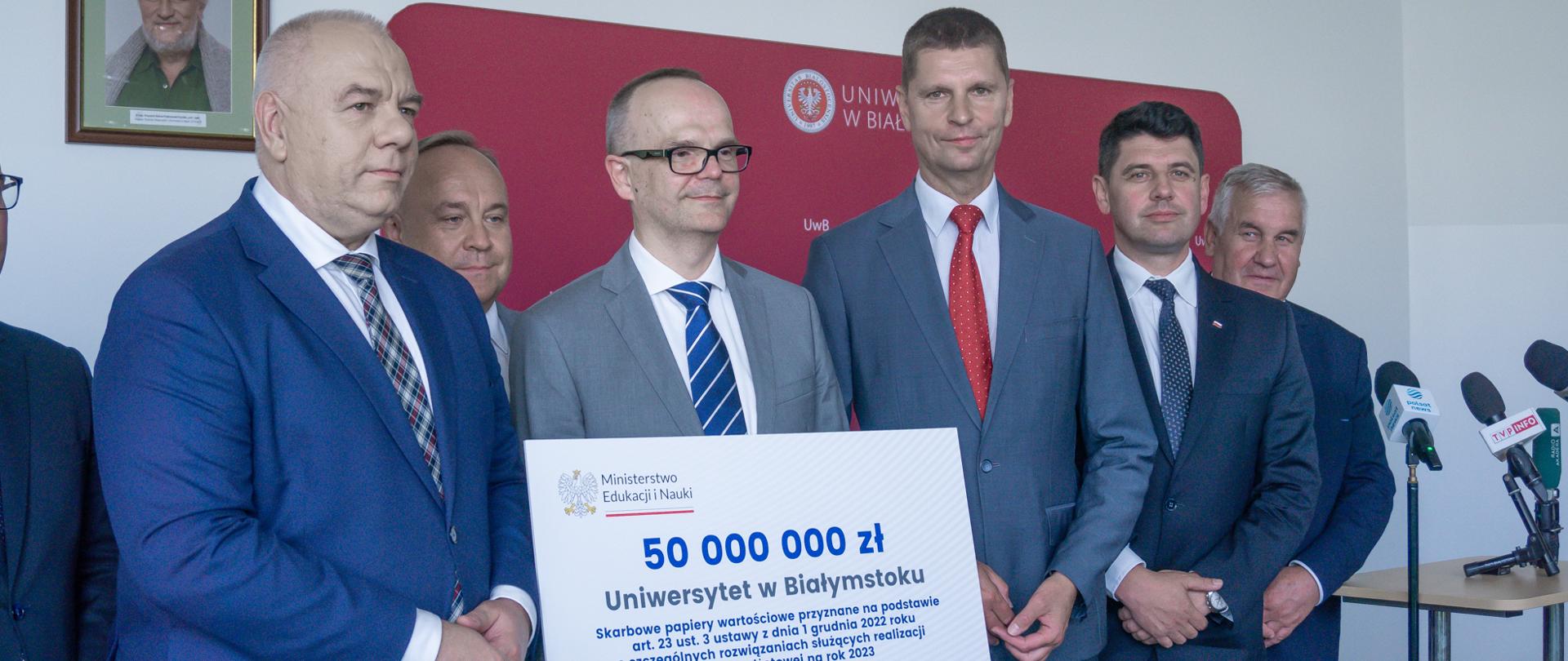 Sześciu mężczyzn w garniturach. W środku mężczyzna trzyma duży karton z napisem 50 000 000 Uniwersytet w Białymstoku.