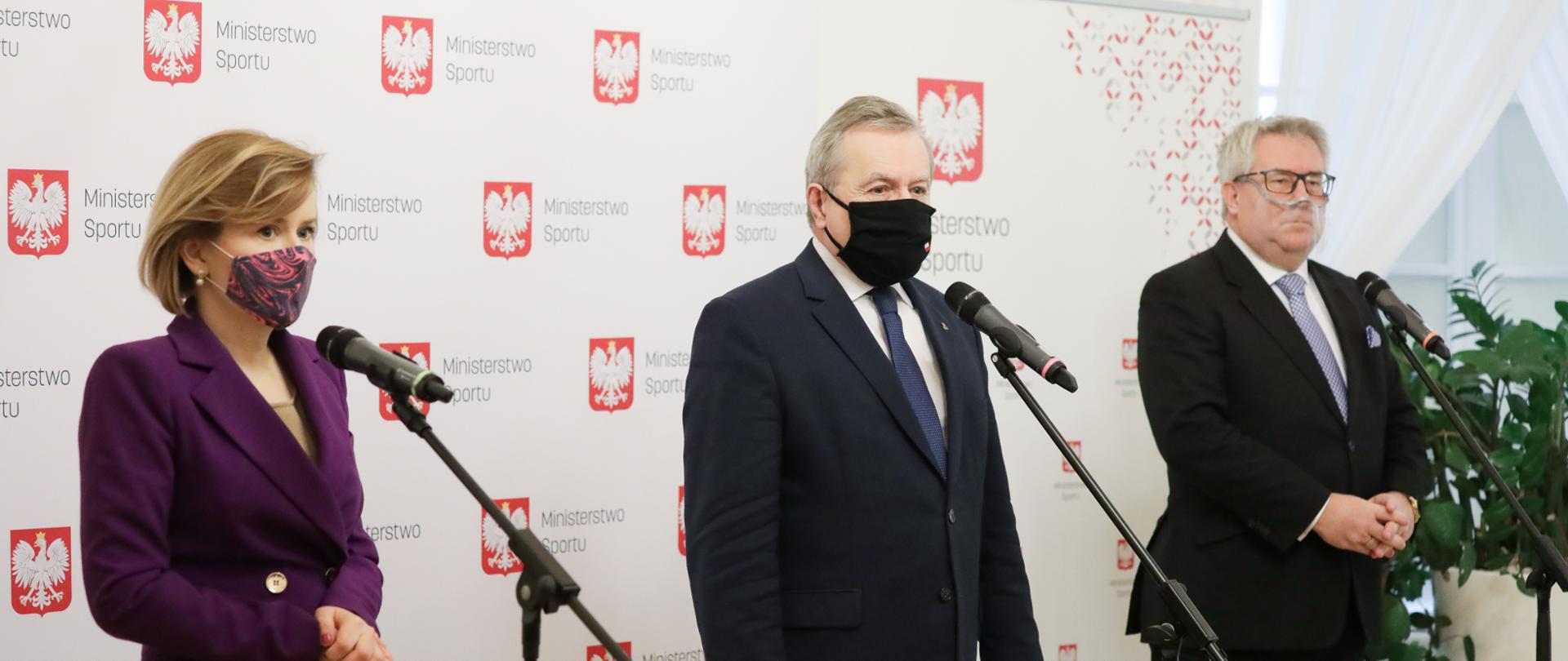 Uczestnicy konferencji prasowej stoją przed mikrofonami.