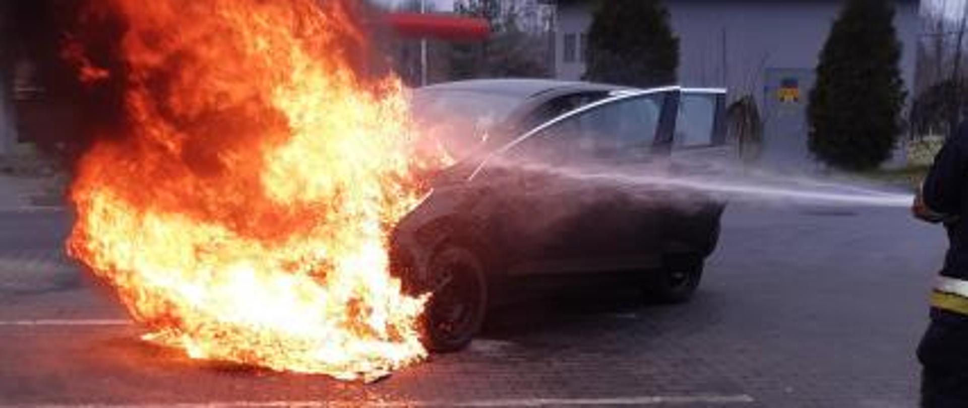 Na zdjęciu samochód osobowy objęty pożarem. Straż Pożarna podaje prąd gaśniczy wody
