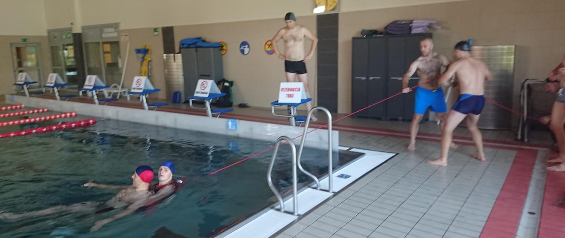 Strażacy przy użyciu sprzętu do ratownictwa wodnego holują poszkodowanego do brzegu.