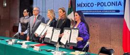 En la foto se ve a cinco personas de pie en fila, de frente a la cámara.
De izquierda a derecha están: la diputada Genoveva Huerta Villegas, el diputado Pedro Vázquez González, la embajadora de Polonia Agnieszka Frydrychowicz-Tekieli, la diputada María Angélica Granados Trespalacios y la diputada Alma Lidia De la Vega Sánchez.
Todos visten de manera elegante, con trajes o vestidos formales. Los participantes tienen expresiones tranquilas y concentradas, y algunos sonríen levemente. Al fondo se ve la sala del Parlamento con los emblemas y banderas de México, lo que le da a la escena un carácter solemne y oficial.
La foto muestra el momento de la instalación del Grupo de Amistad México-Polonia.