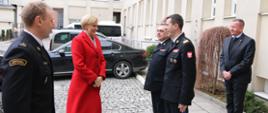 Przywitanie Pierwszej Damy. Na placu wewnętrznym Szkoły w czerwonym płaszczu Pani Prezydentowa. Obok niej witający ją strażacy w mundurach wyjściowych. Komendant Główny PSP nadbryg. Mariusz Feltynowski, Zastępca Komendanta Głównego PSP nadbryg. Józef Galica, p.o. Komendant Szkoły Aspirantów PSP w Krakowie mł.bryg. Dariusz Ruchała