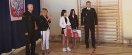 Komendant Powiatowy PSP w Kozienicach i Dowódca JRG Kozienice podczas uroczystego rozpoczęcia roku szkolnego w sali gimnastycznej w SP w Janikowie wręczają uroczyście podziękowania za bohaterską postawę uczennic