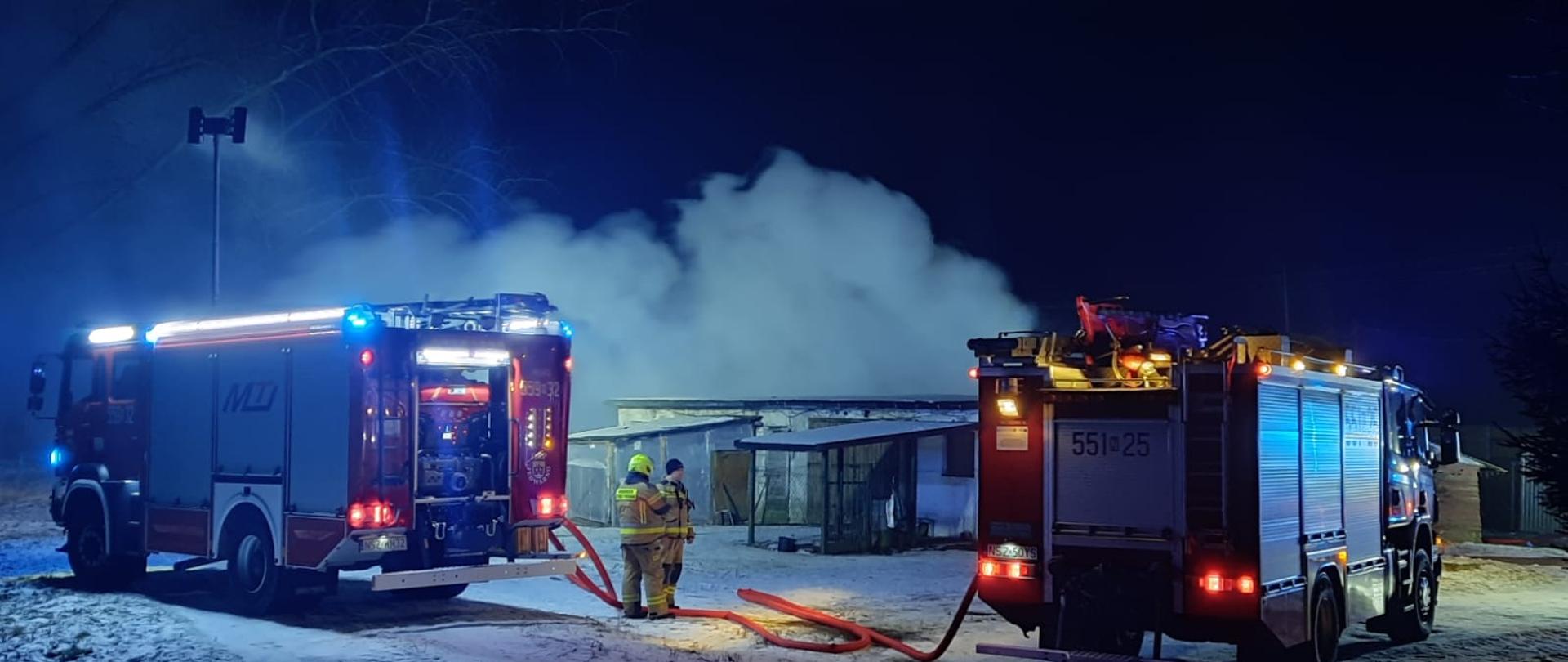 Zdjęcie przedstawia strażaków oraz samochody pożarnicze na tle pożaru budynku gospodarczego w miejscowości Lipniki