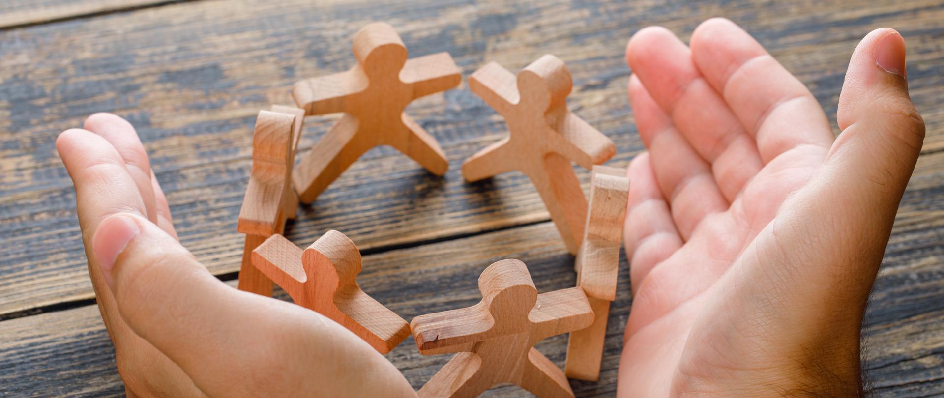 Koncepcja sukcesu biznesowego na drewnianym tle, widok z wysokiego kąta. ręce chroniące drewniane postacie ludzi. 