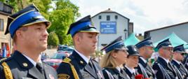 Strażacy w galowych mundurach ustawieni w szeregu. Kobiety w galowych mundurach stojące w szeregu trzymają czerwone róże.