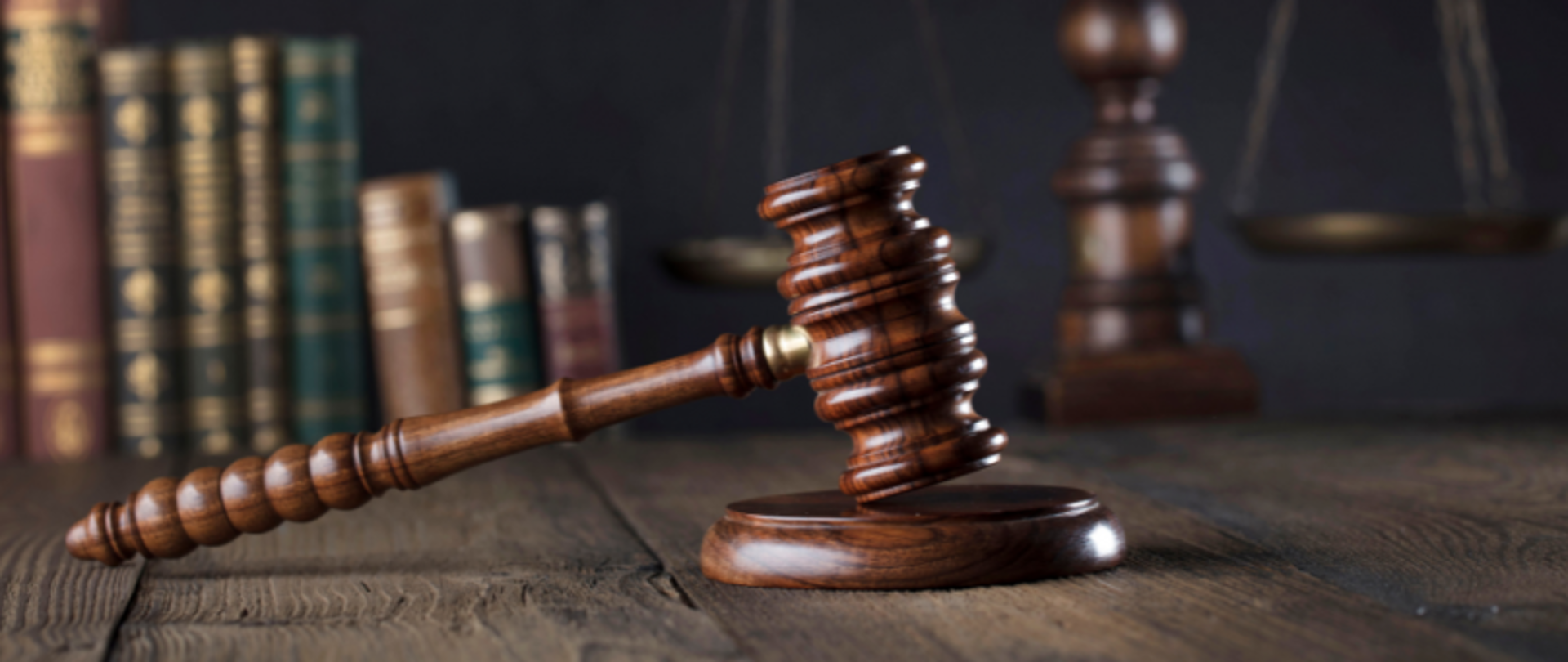 Blat biurka. Na nim młotek sędziowski na podstawce. W tle książki.