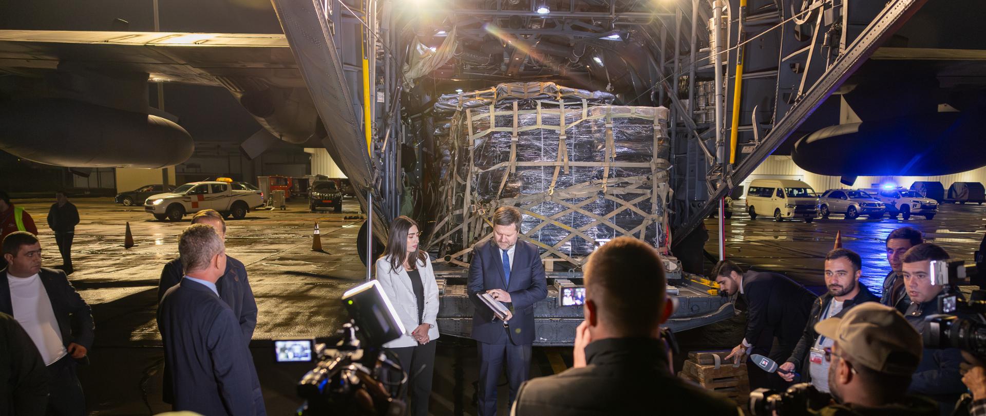 Mężczyzna i kobieta stoją przed załadunkiem w samolocie, grupa osób stoi przed nimi.