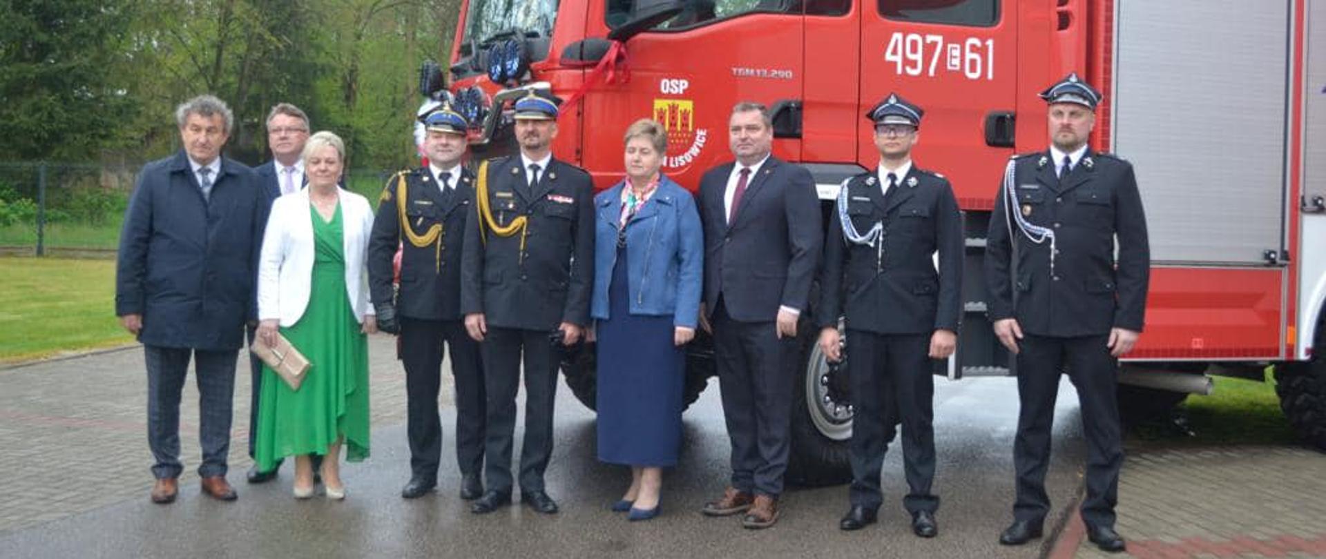 strażacy druhowie politycy i samorządowcy pozują do zdjęcia na tle samochodu pożarniczego