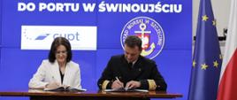 Dyrektor Centrum Unijnych Projektów Transportowych Joanna Lech i Dyrektor Urzędu Morskiego w Szczecinie Wojciech Zdanowicz siedzą przy stole i podpisują dokumenty umowy, za ich plecami grafika informująca o podpisaniu pre-umowy o finansowaniu budowy nowego toru podejściowego w porcie Świnoujście
