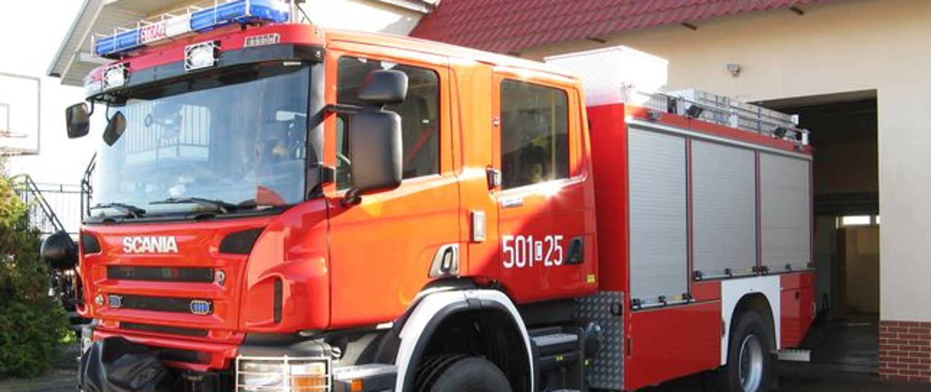 Zdjęcie przedstawia ciężki samochód ratowniczo - gaśniczy ze zbiornikiem wodnym i sprzętem ratowniczym marki SCANIA, w kolorze czerwonym, na tle garażu KP PSP.