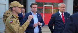 Na zdjęciu widać KP PSP w Zgierzu oprowadzającego gości po terenie jednostki , w tle czerwone bramy garażowe JRG w Zgierzu. 