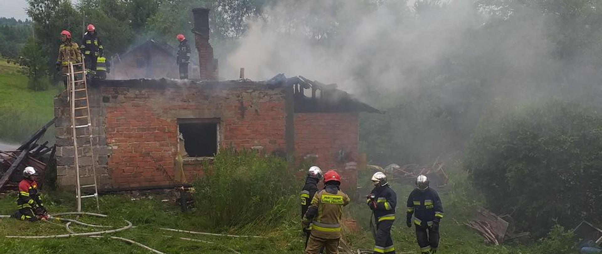 Dym wydobywający się z budynku oraz strażacy gaszący pożar.