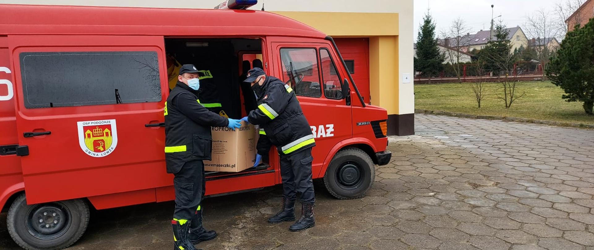 dwóch strażaków pakuje maseczki ochronne do samochodu strażackiego