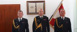 Zdjęcie przedstawia trzech funkcjonariuszy Państwowej straży Pożarnej w mundurach wyjściowych ze sznurem galowym. W środku Komendant Wojewódzki PSP po obu stronach funkcjonariusze, którzy odbierali akty powołania na kierownicze stanowisko w jednostkach organizacyjnych PSP