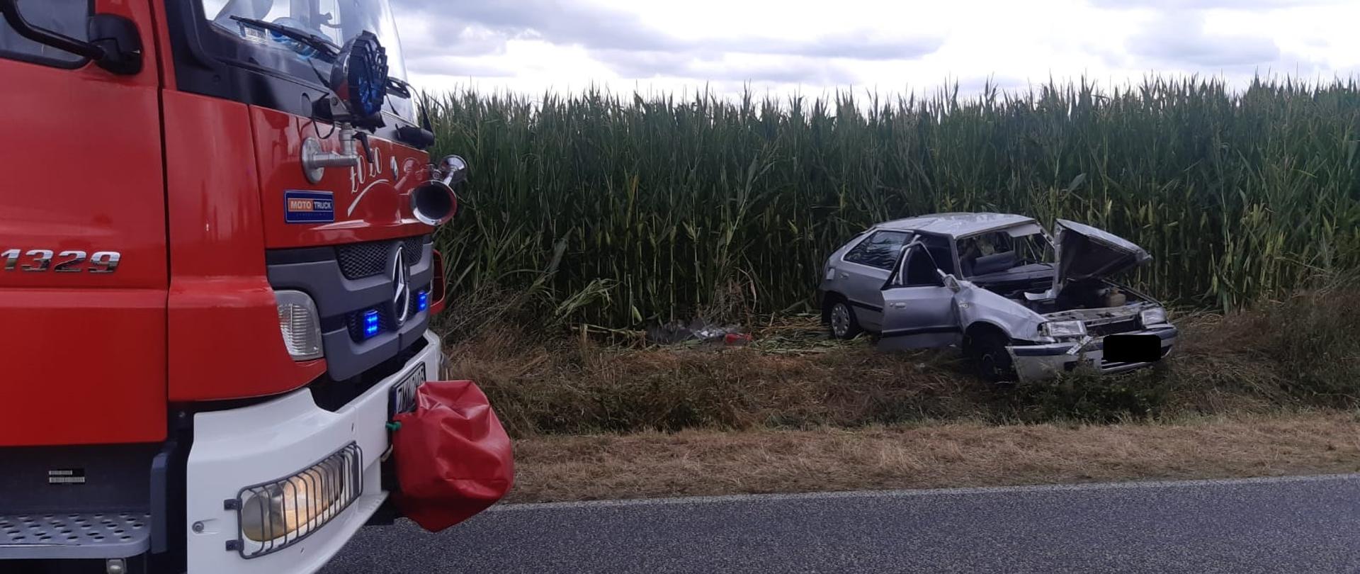 W tle widać rozbity samochód osobowy znajdujący się częściowo na polu kukurydzy